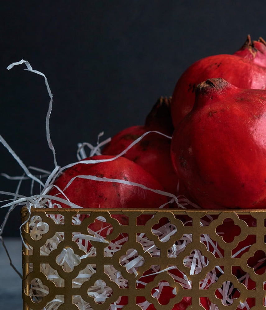Close-up of a decorative golden basket filled with fresh red pomegranates and white filling material against a dark background