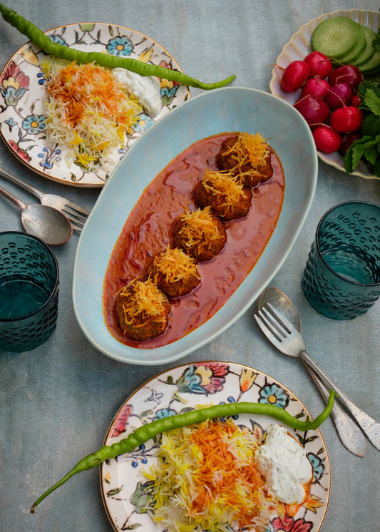 Five meatballs in red tomato sauce on a blue plate, served with seasoned rice, yogurt and green chili on decorative plates
