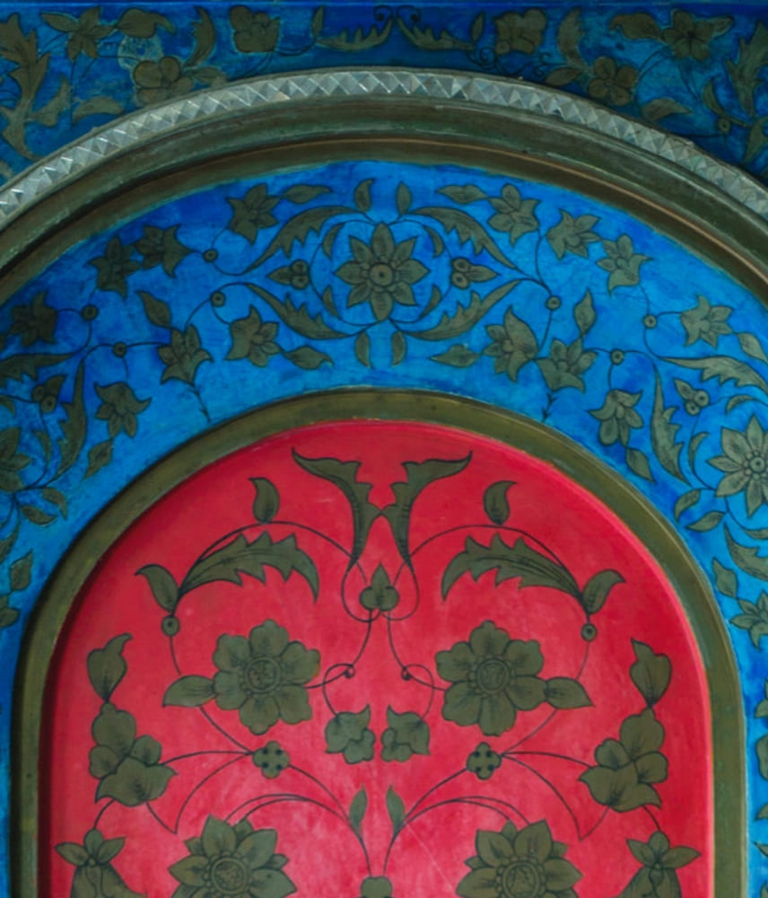 Close-up of an artistically painted wall with oriental floral patterns in blue and red, framed by decorative arches.