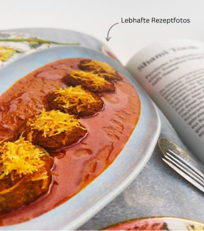 Close-up of a Persian cookbook with a vibrant photo of Shami Tabrizi in tomato sauce and golden garnish on a blue plate, next to recipe text and cutlery