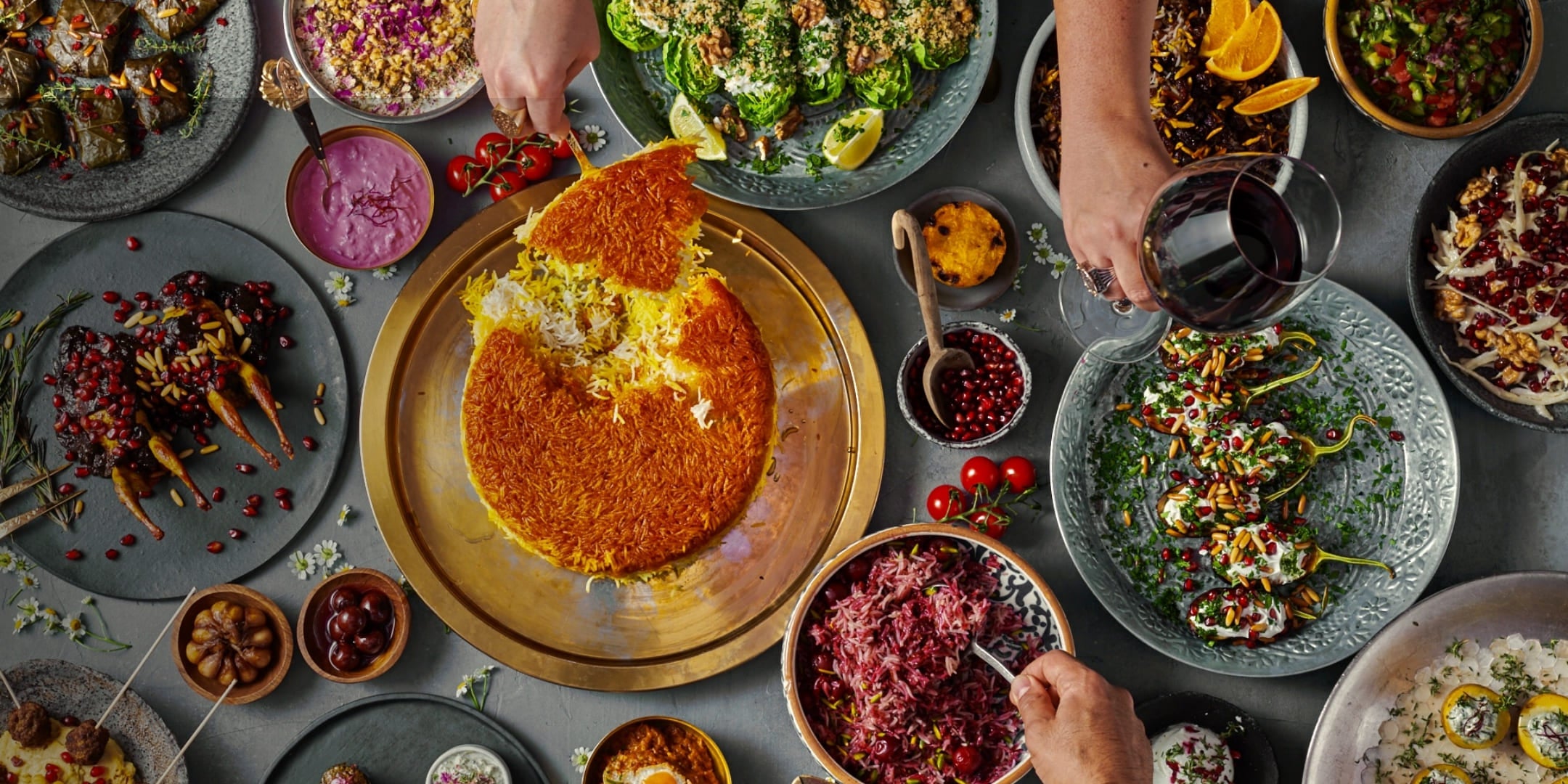 Traditional Persian table with saffron tahdig, stuffed eggplants, herbs, pomegranate, and various oriental appetizers served on decorative plates.